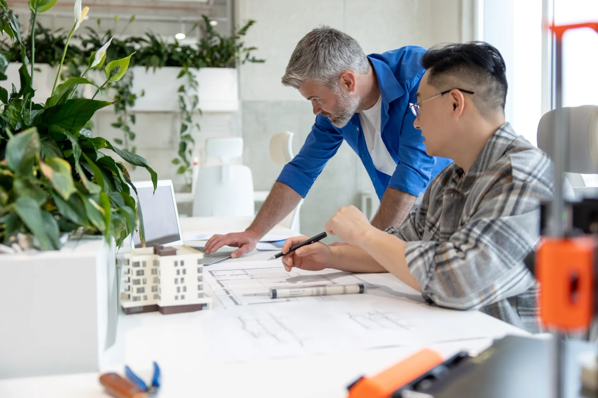 Designer and architect reviewing a printed floor plan beside a building model